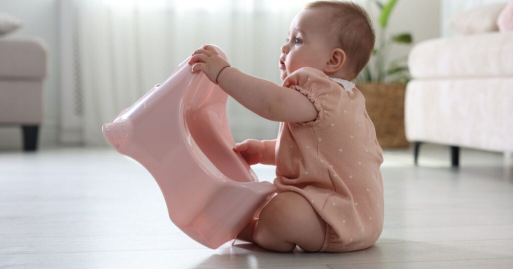 elimination-communication-baby-sitting-on-the-floor-holding-a-pink-potty