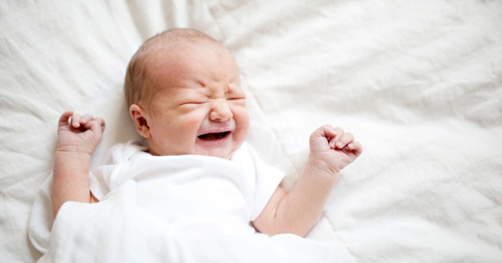 baby-sleep-baby-laying-on-white-sheet-crying-from-lack-of-sleep
