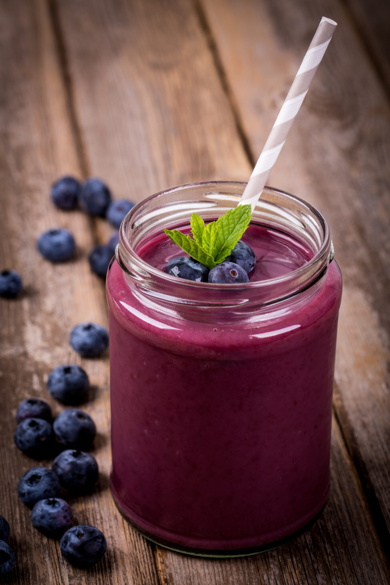 Blueberry smoothie in a glass jar with a straw and sprig of mint