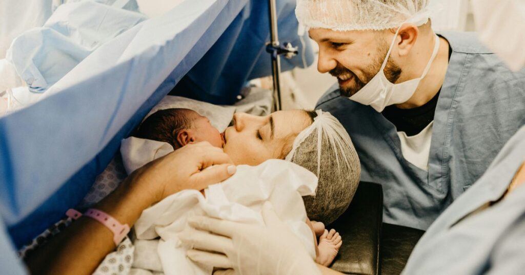 woman who gave birth in hospital holding her newborn baby with her partner smiling next to her