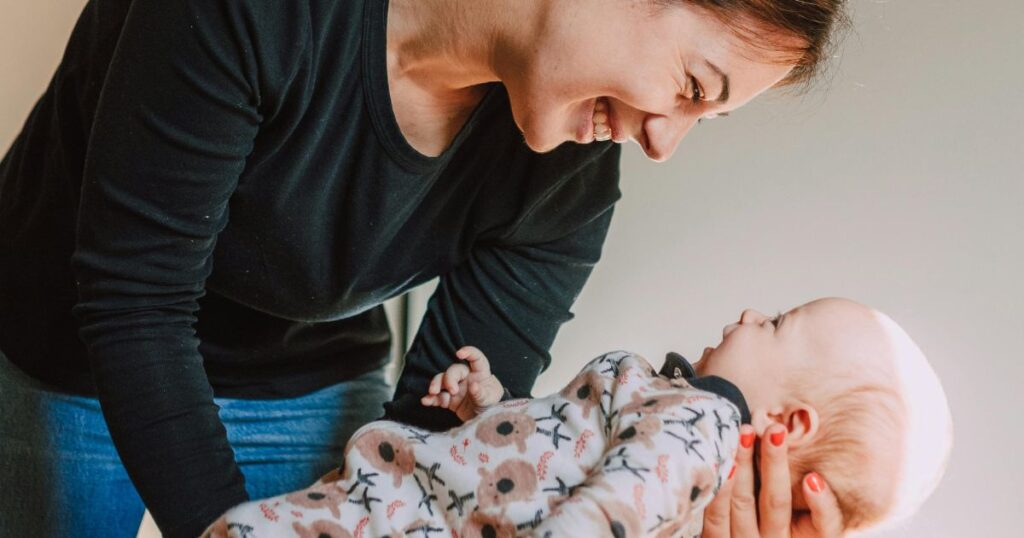 mom standing, holding her smiling baby and smiling back down at them