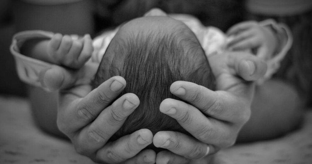 parent holding their newborn baby's head in both hands while baby is lying down