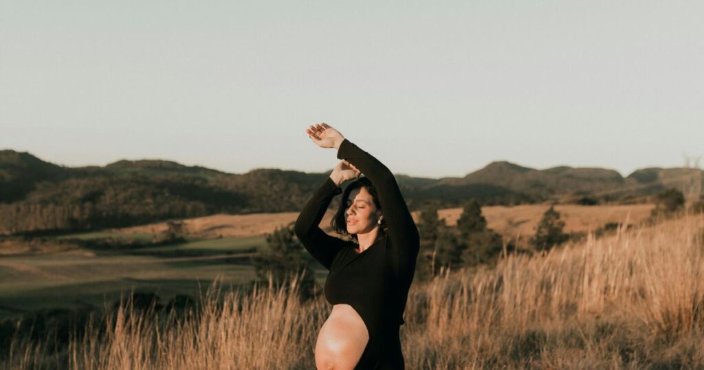 Pregnant-woman-in-black-dress-posing-outdoors-in-a-field-near-Charlotte-NC-maternity-photography-at-sunset