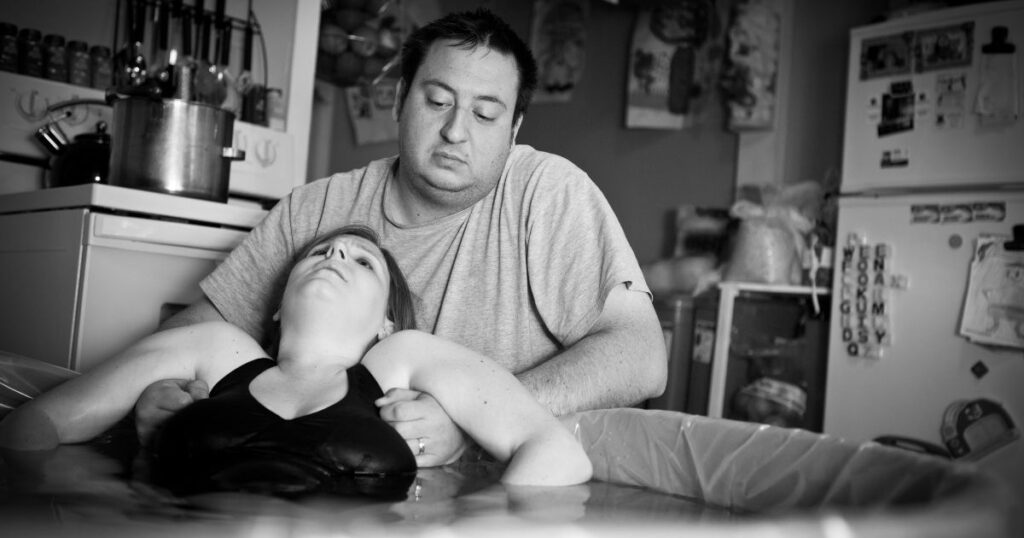 laboring person in water birth tub in charlotte NC with partner supporting them from behind