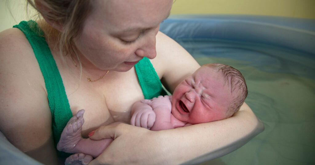 New birthing parent holding newborn in water birth tub at birth center in charlotte, NC