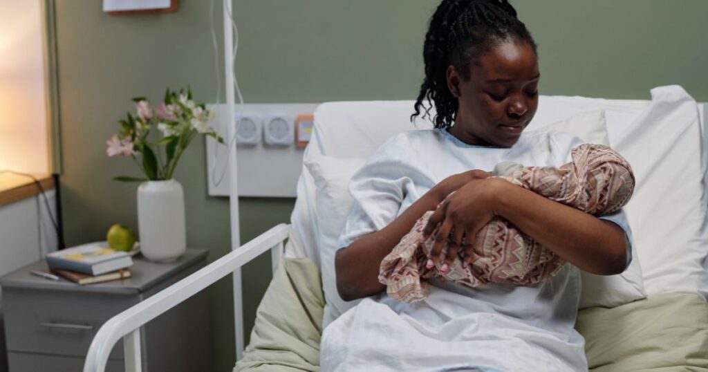 newly postpartum mother sitting in a hospital bed holding her newborn baby wrapped in a blanket