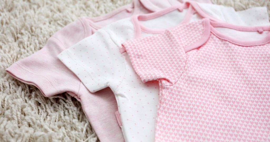 three pink newborn baby onesies neatly laid out on a carpet