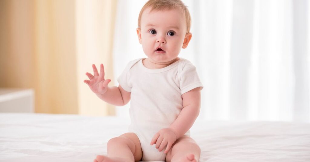 Baby sitting in white sheet bed