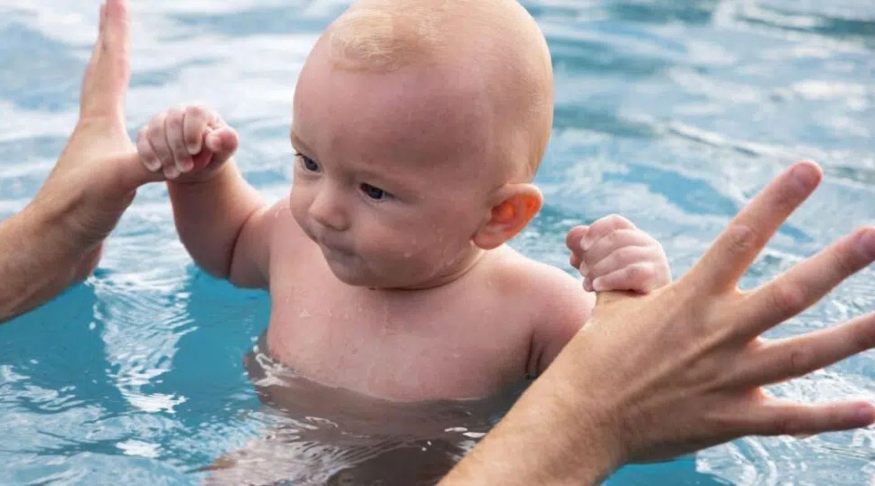 Baby swimming holding hands for support