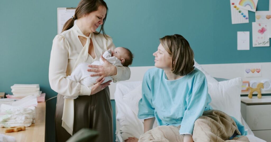 Mom in the bed, looking at her newborn being carried