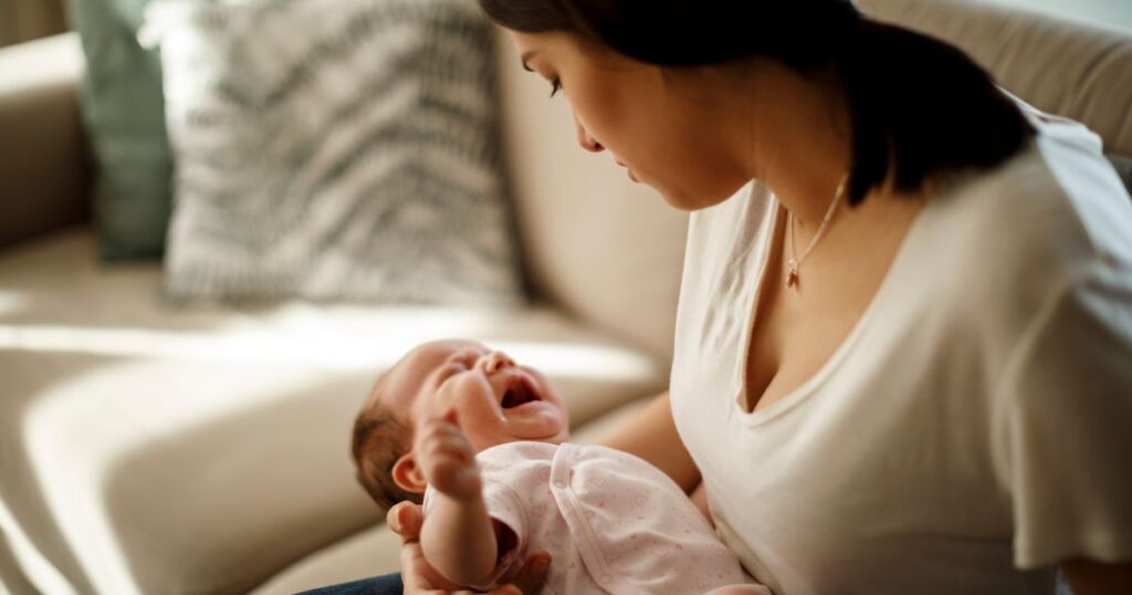 mother sitting on a white couch holding her crying newborn baby in her arms