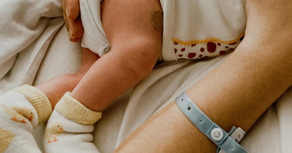 newly postpartum mother with identification tag on her wrist, holding her newborn baby