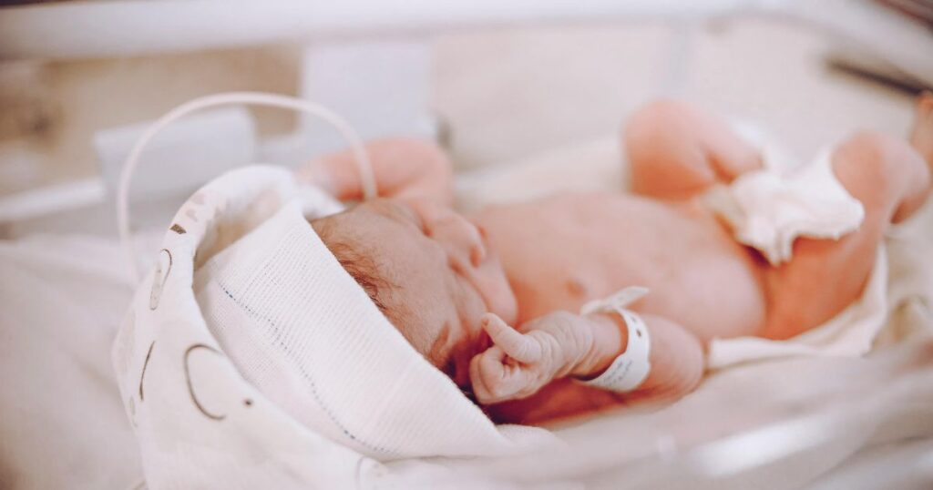 newborn baby with white cap lying in a hospital bassinet