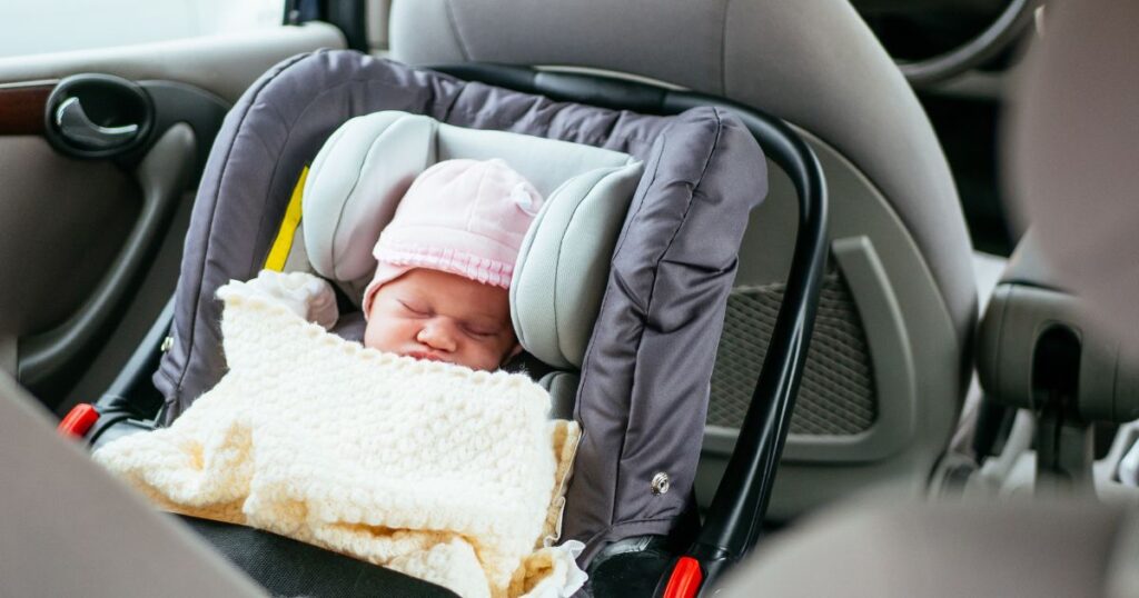 newborn baby asleep in a car seat under a blanket on the way home from the hospital