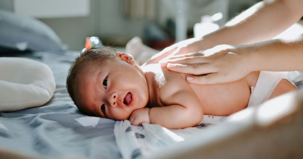 newborn baby lying on their stomach while postpartum doula is rubbing their back