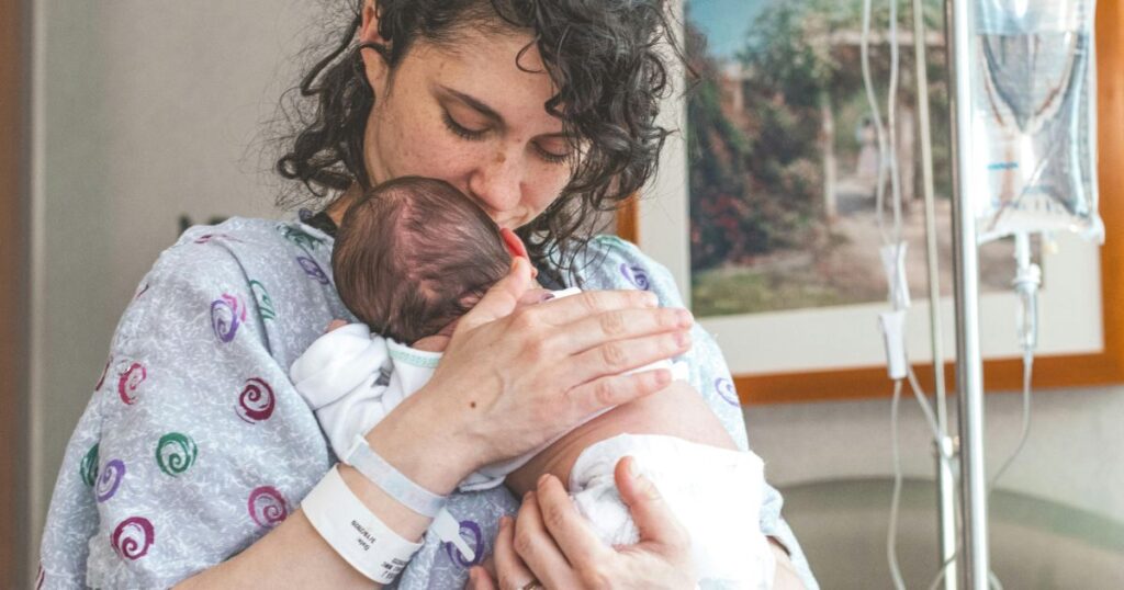 newly postpartum mother in hospital holding and kissing her baby