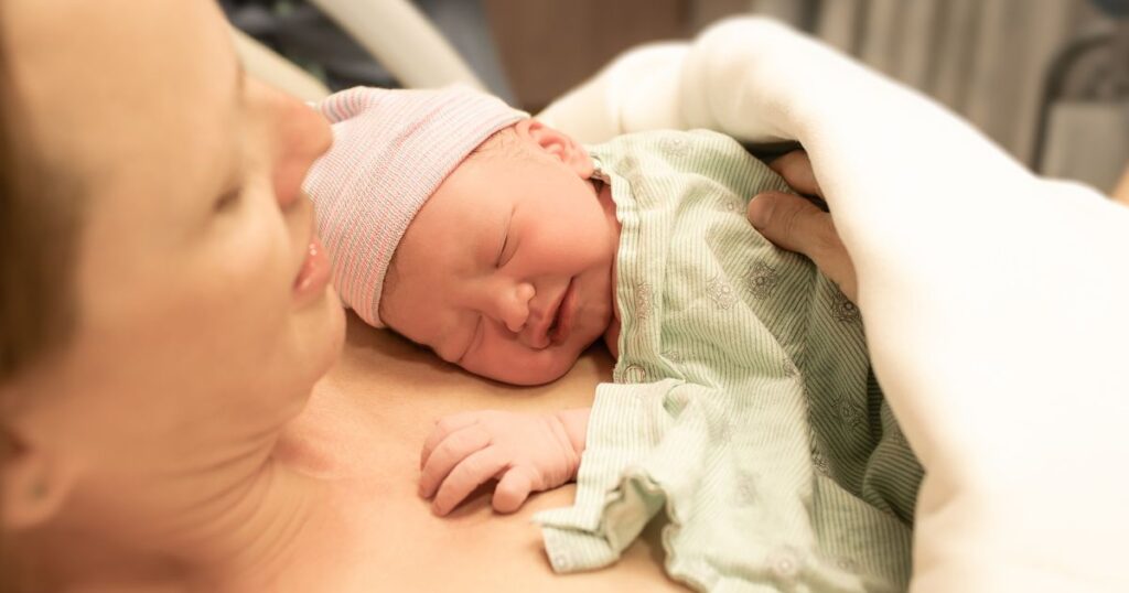 postpartum mother holding her newborn baby under a blanket after giving birth