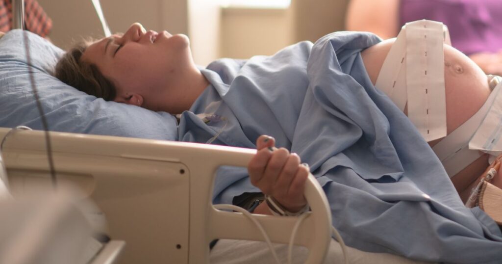 pregnant woman lying in a hospital bed in intense labor, holding onto the bed's side rails