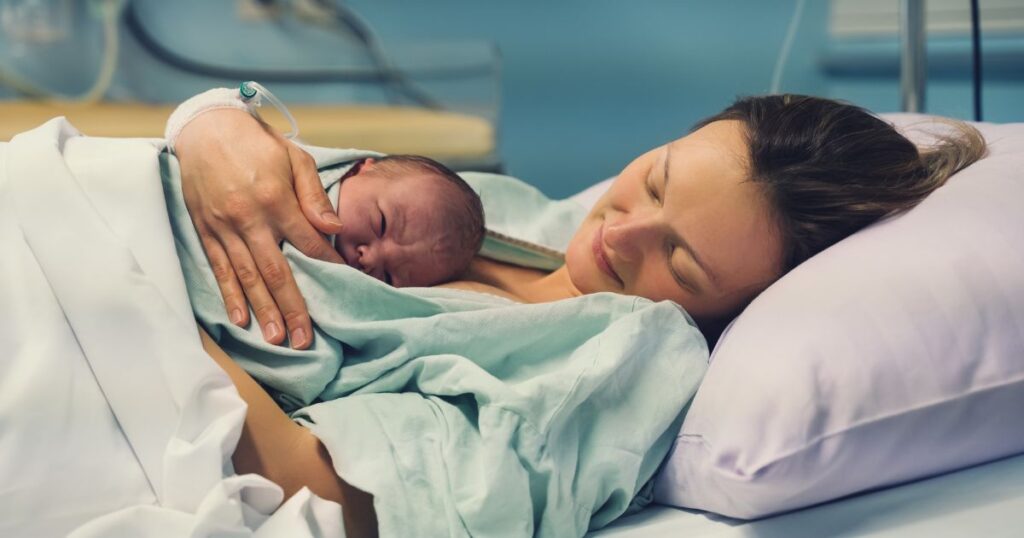 newly postpartum mom smiling while lying in a hospital bed holding her newborn baby on her chest
