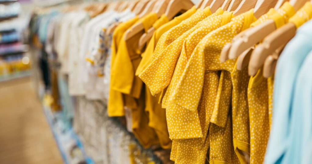 yellow and white baby clothes hanging on wooden hangers inside a store