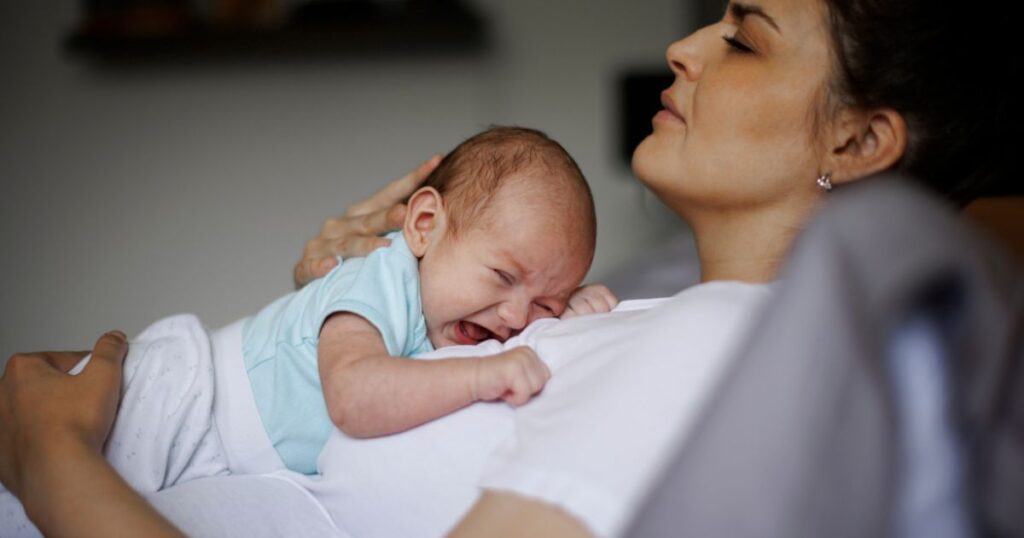 mother lying down while gently holding newborn baby on her chest as baby cries
