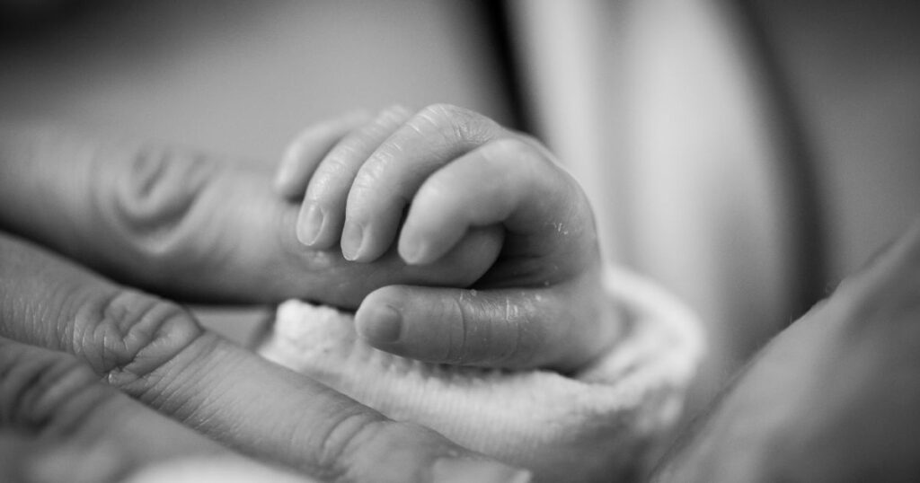 black and white photo of newborn baby's hand, holding onto their parent's finger