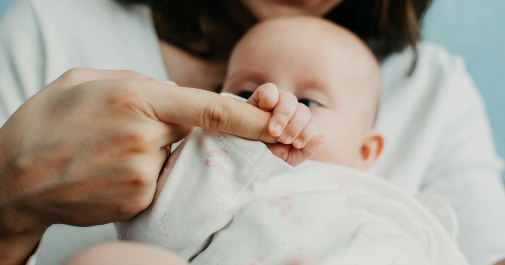 newborn baby wrapped in a blanket holds onto their parent's finger