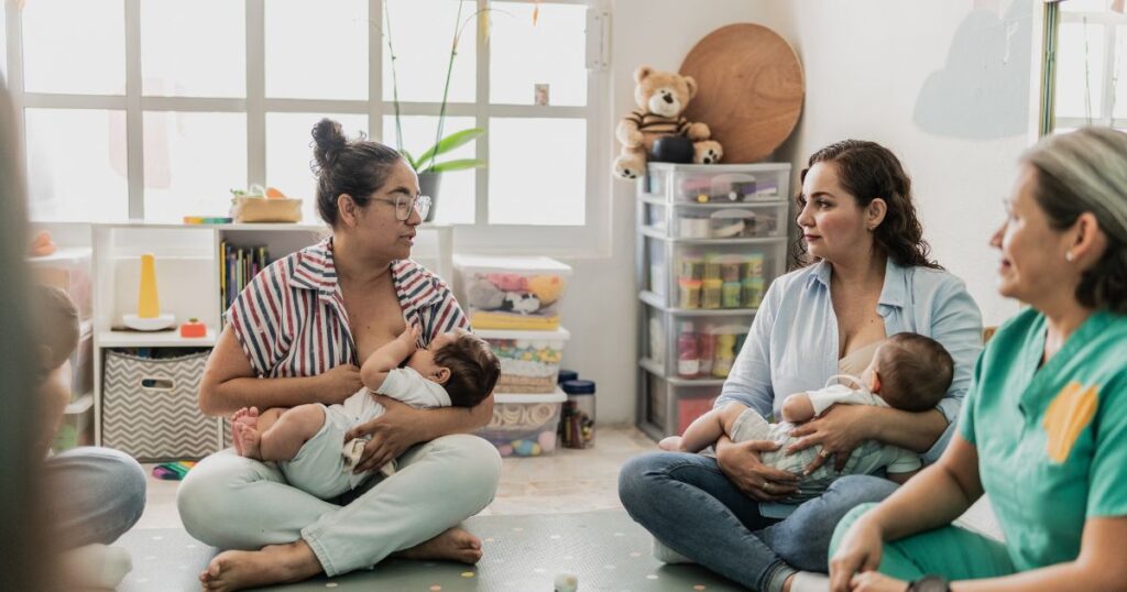 mothers sitting on the floor in a breastfeeding support group talking to each other while one mother feeds her baby