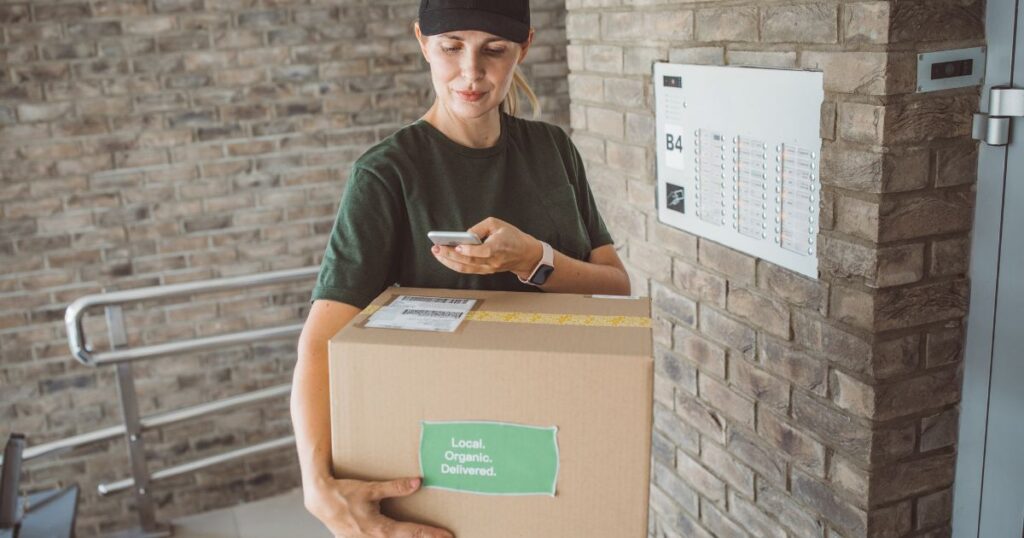 meal delivery woman standing in front of an apartment building, holding a delivery box as she scans the barcode
