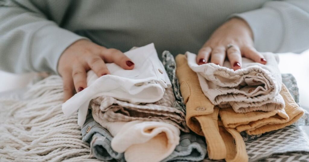 woman with red nail polish resting her hands on neatly folded, clean baby clothes