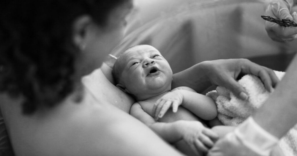 black and white photo of a newly postpartum mother holding her baby after giving birth in a birthing tub