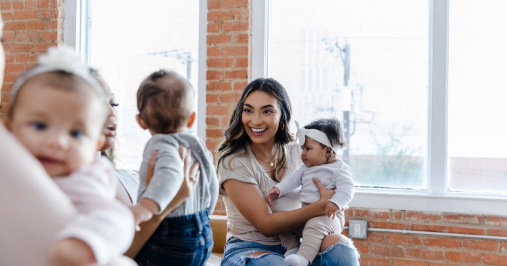 woman smiling and holding her baby while chatting to moms at a mom support group