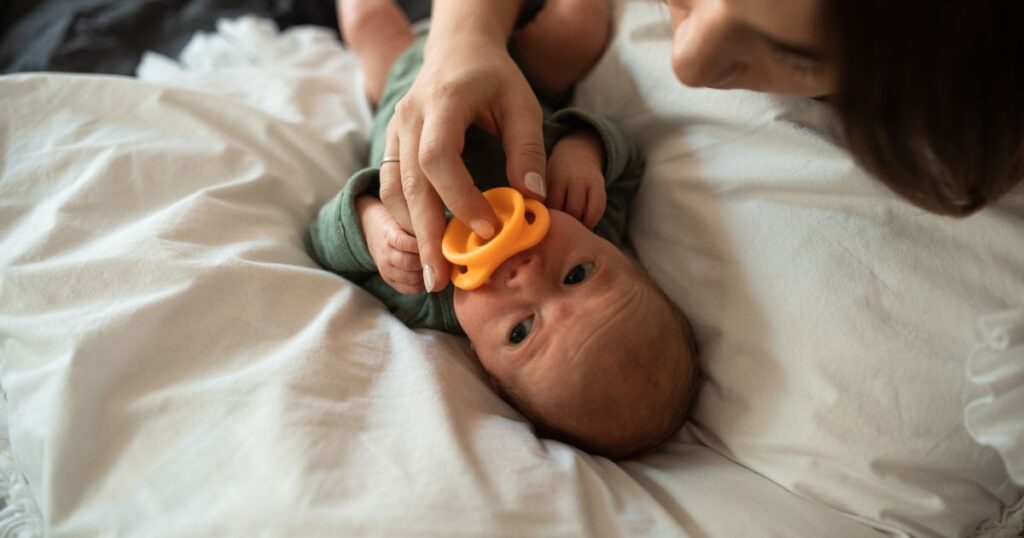 mother lying on the bed with her newborn baby, holding a dummy in baby's mouth
