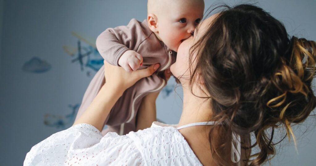 mother smiling whole she holds her baby above her head and gives them gentle kisses