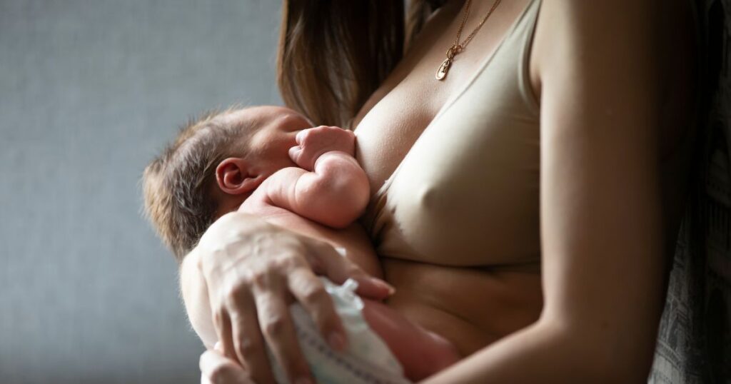 mother wearing a nursing bra holds her newborn baby while baby is breastfeeding