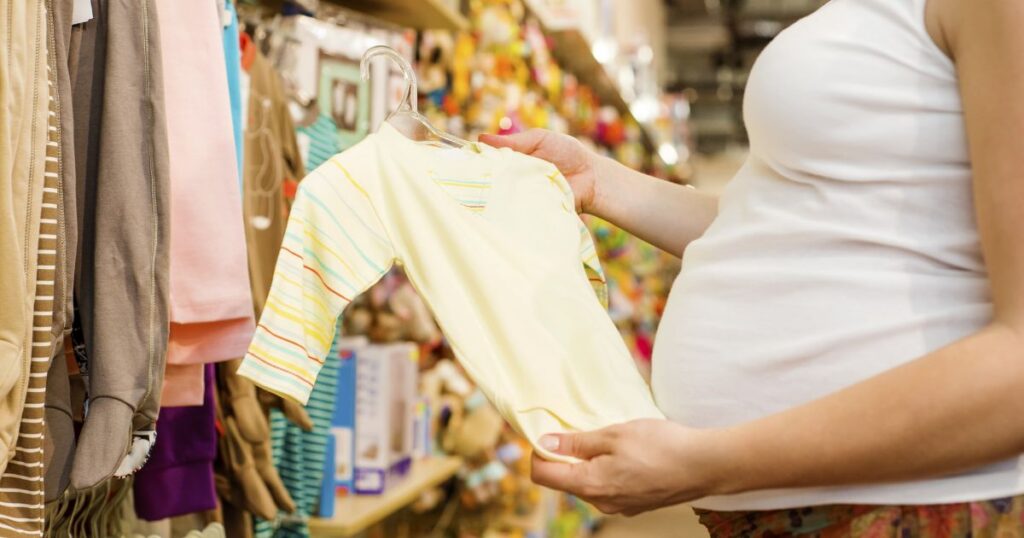 pregnant mother shopping for baby clothes, holding a pastel yellow baby onesie