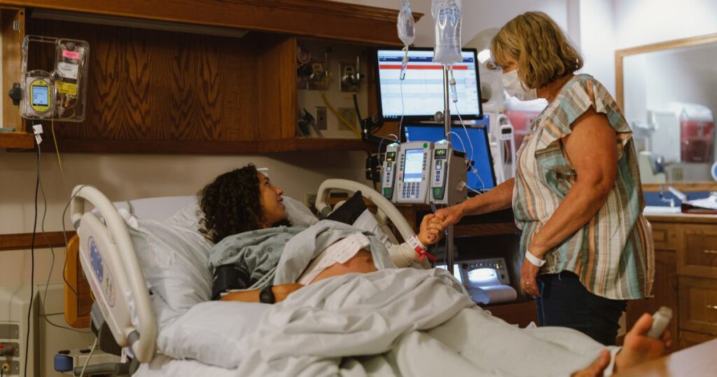 pregnant woman lying in a hospital bed, waiting to give birth while holding an older woman's hand for support
